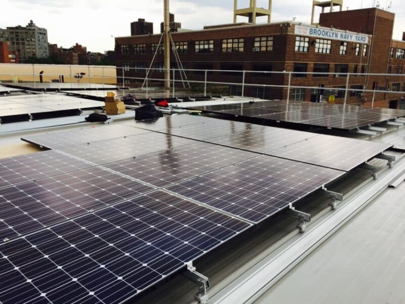 Solar panels in foreground, brick building behind with text: Brooklyn Navy Yard